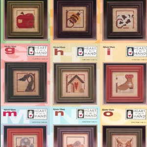 Puede incluir: Una colecci&oacute;n de bordados de punto de cruz enmarcados con varios dise&ntilde;os, incluyendo una manzana, una abeja y una vaca. Cada bordado est&aacute; en un marco cuadrado con un borde oscuro. El texto "Alphabet Mania" y "Heart in Hand" es visible.