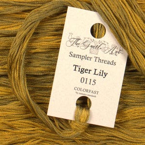 May include: A skein of The Gentle Art Sampler Threads in the color Tiger Lily, color number 0115. The label is white with black text and says "Sampler Threads", "Tiger Lily", "0115", and "COLORFAST by industry standards".
