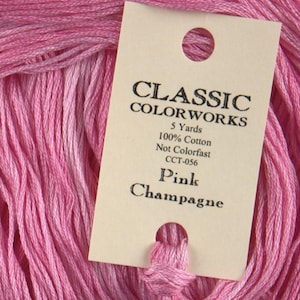 Pode incluir: Um novelo de fio de bordar de algodão rosa com um rótulo que diz "CLASSIC COLORWORKS 5 Yards 100% Cotton Not Colorfast CCT-056 Pink Champagne".