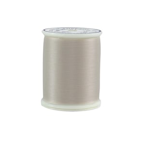 Könnte beinhalten: Eine Spule hellbeige Garn. Das Garn ist eng um eine weiße Kunststoffspule gewickelt. Die Oberseite der Spule hat ein weißes Etikett mit blauem Text. Das Garn hat einen subtilen Glanz, der auf eine glatte Textur hindeutet.
