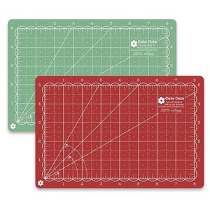 May include: Two self-healing cutting mats, one green and one red, with a grid pattern and numbers 1 through 8 along the edges. The mats are labeled "Cute Cuts by Lori Holt of Bee in my Bonnet" with a small flower graphic.