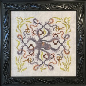 Puede incluir: Obra de arte de punto de cruz de un pulpo en tonos grises, marrones y melocotón, rodeado de algas marinas y elementos decorativos. La obra está enmarcada en un marco negro ornamentado, añadiendo un toque de elegancia. El diseño es intrincado y detallado.