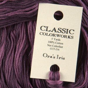 Op de afbeelding: Een klosje paarse borduurgaren met het label "Classic Colorworks" en de kleurnaam "Ora's Iris".  Details over het garen: 5 yards, 100% katoen, niet kleurvast, CCT-216.