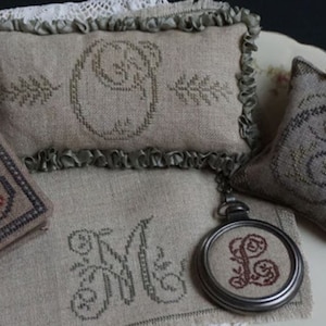 May include: A set of four embroidered pillows with different letters, each with a floral design. The pillows are made of a light brown fabric and have a rustic look. The pillows are arranged on a white surface with a floral pattern.