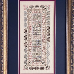 May include: A framed cross-stitch sampler with a white background and colourful embroidery. The sampler features a variety of designs, including flowers, trees, and letters. The text on the sampler reads "Caz friendship Saraen 2010" and "H I J K L M N O P Q R S T U".