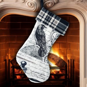 May include: A Christmas stocking with a black and white raven illustration and script design. The top cuff features a black, white, and gray plaid pattern. The stocking is hanging in front of a fireplace.