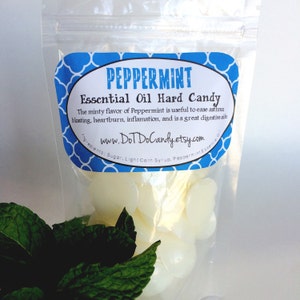 May include: A clear plastic bag filled with white peppermint hard candies. The bag has a blue and white label that reads "PEPPERMINT Essential Oil Hard Candy" and "www.DoDoCandy.etsy.com". A sprig of fresh green mint leaves is in the foreground.