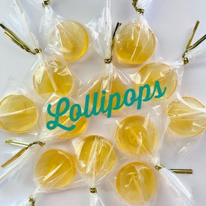May include: A close-up of a group of round, clear, yellow lollipops wrapped in cellophane with gold ribbon and white sticks. The lollipops are arranged in a circle with the text "Lollipops" written in teal cursive in the center. The text "Do T Do Candy" is written in black at the bottom of the image.