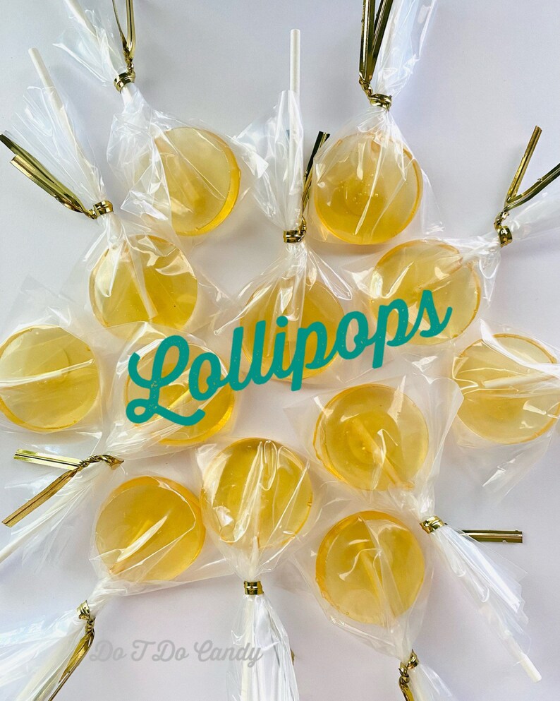 May include: A close-up of a group of round, clear, yellow lollipops wrapped in cellophane with gold ribbon and white sticks. The lollipops are arranged in a circle with the text "Lollipops" written in teal cursive in the center. The text "Do T Do Candy" is written in black at the bottom of the image.