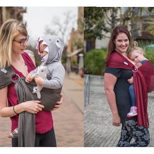 Puede incluir: Dos portabeb&eacute;s en uso. Uno es gris oscuro con un anillo plateado, el otro es burdeos con un anillo dorado. Ambos se utilizan para transportar a ni&ntilde;os peque&ntilde;os. El beb&eacute; del primer portabeb&eacute;s lleva una sudadera con capucha de tibur&oacute;n.