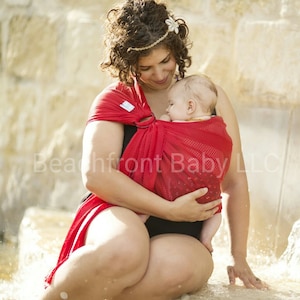 Puede incluir: Un portabeb&eacute;s rojo con un dise&ntilde;o de malla. El portabeb&eacute;s lo lleva una persona con un traje de ba&ntilde;o negro. La imagen incluye el texto "Beachfront Baby LLC".