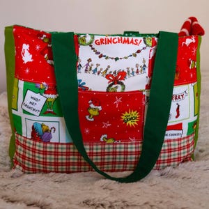 May include: A Grinchmas-themed tote bag with green handles and accents. The bag features a patchwork design with red, white, and green panels. The panels display Grinch-related illustrations and the text "GRINCHMAS".