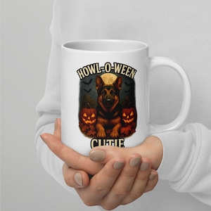 Può includere: Tazza in ceramica bianca con un design di Halloween con un cane pastore tedesco. La tazza ha le parole "Howl-o-ween Cutie" con zucche, pipistrelli e una luna piena.