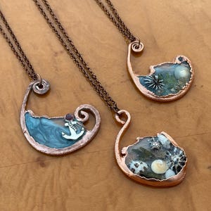 May include: Three handcrafted copper necklaces with unique ocean-themed pendants. Each pendant features a different design: swirling blue resin with an anchor, a miniature sea scene, and a collection of seashells and a turtle. The necklaces have copper chains.