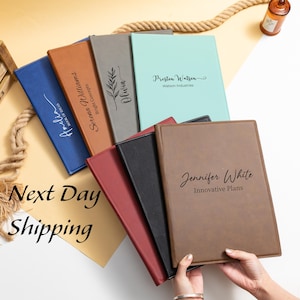 May include: A collection of personalized leather portfolios in various colors, including blue, brown, and black. Each portfolio features custom text, such as names and company names. The words "Next Day Shipping" are also visible.