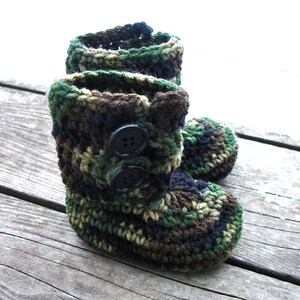 Puede incluir: Botas de bebé de crochet de camuflaje con botones negros. Las botas están hechas con hilo verde, marrón y negro.