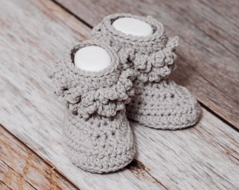 Könnte beinhalten: Ein Paar graue gehäkelte Babyschuhe mit Rüschen.