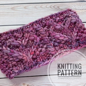 May include: A chunky knit headband in shades of purple and pink. The headband features a cable knit design and is made of thick, textured yarn. The text "Knitting Pattern" is visible in the lower right corner.