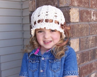 May include: A young person wearing a white crocheted hat with a brown ribbon and a denim shirt.