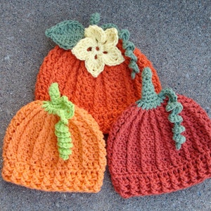 May include: Three crocheted pumpkin hats in orange and green. The hats have a stem and leaf detail.