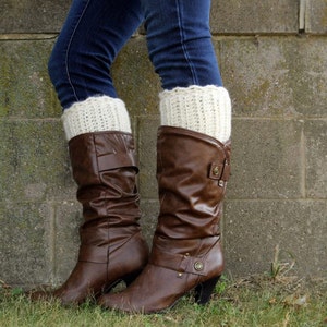 May include: Brown leather boots with white crocheted leg warmers. The boots have a buckle detail and a low heel.