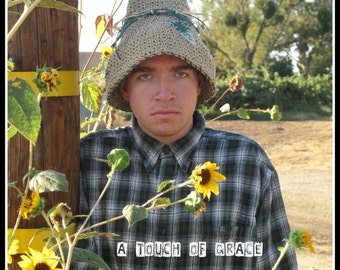 May include: A beige crocheted pointed hat with a dark green cord tied around the base, worn with a black and white plaid long-sleeve button-down shirt. The text A TOUCH OF GRACE is printed in white on the front of the shirt chest area.
