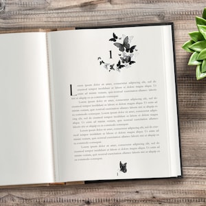 May include: An open book with a black cover, showing a page with text and a butterfly design. The butterflies are grey and clustered around the number "1". The opposite page is blank, with a wooden background.