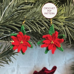 Op de afbeelding: Een paar handgemaakte gehaakte oorbellen in de vorm van poinsettia's. De oorbellen hebben helderrode bloemblaadjes, groene bladeren en goudkleurige kralenmiddens. De tekst "CROCHET PDF PATTERN" staat in een witte cirkel. De oorbellen hangen aan goudkleurige haken.
