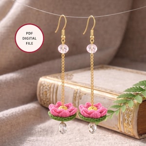 Könnte beinhalten: Handgefertigte Ohrringe mit gehäkelten rosa Lotusblüten und grünen Basen, die an goldfarbenen Ketten hängen. Jeder Ohrring hat einen klaren Kristall am unteren Ende und eine rosa Perle am oberen Ende. Das Bild enthält auch eine Grafik "PDF DIGITAL FILE".