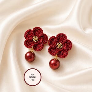 May include: A pair of handmade, dark red crochet flower earrings with gold-colored centers and a dangling dark red pearl. The earrings are displayed on a cream-colored satin fabric. The earrings are a PDF digital file.
