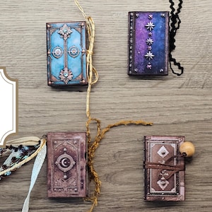 May include: Four printable fairy mini books for junk journals. The books have ornate covers in shades of blue, purple, and brown, with decorative elements. The text on the image reads "4 Printable Fairy Mini Books For Your Junk Journal."
