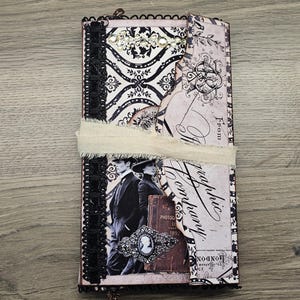 May include: A vintage-style journal with a black and white damask pattern, embellished with black lace trim and a cream-colored ribbon. The cover features a sepia-toned image of a couple and decorative elements.