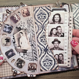 May include: Vintage-style scrapbook with a decorative wheel of small photos and a strip of film-like images. The pages feature patterned paper in shades of gray and blue, creating a nostalgic feel. The scrapbook is open, revealing the contents.