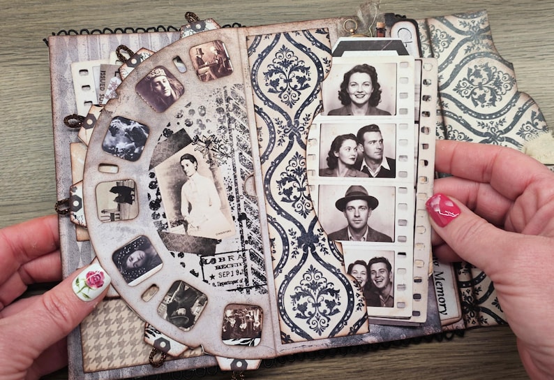 May include: Vintage-style scrapbook with a decorative wheel of small photos and a strip of film-like images. The pages feature patterned paper in shades of gray and blue, creating a nostalgic feel. The scrapbook is open, revealing the contents.