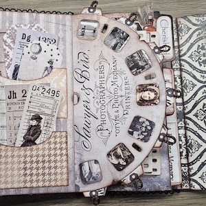 May include: A vintage-style scrapbook with a decorative cover and pages. The scrapbook features a film reel design with old photographs, tickets, and patterned paper. The text "Sawyer & Bird, Photographers" is visible.
