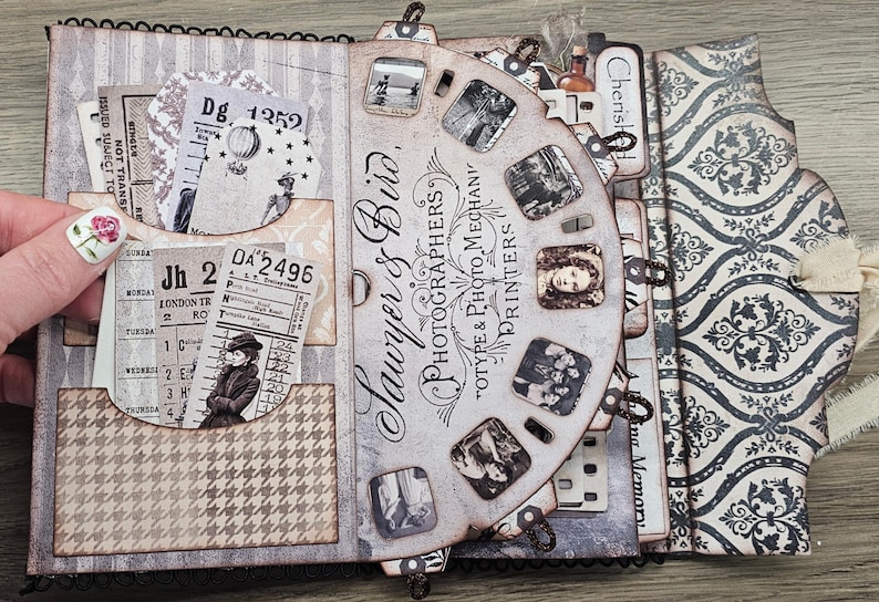 May include: A vintage-style scrapbook with a decorative cover and pages. The scrapbook features a film reel design with old photographs, tickets, and patterned paper. The text "Sawyer & Bird, Photographers" is visible.
