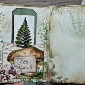 May include: A handmade greeting card featuring a botanical theme with a fern, mushroom, and daisy illustrations. The card includes a small tag with the text Little Moments, a vintage-style key, and a purple bottle graphic on a cream background.