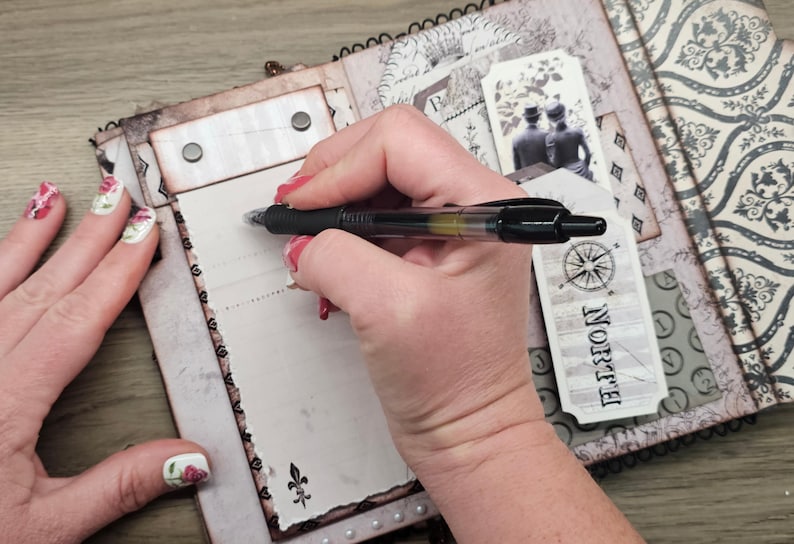 May include: A black pen writing on a vintage-style journal. The journal has a decorative cover with a compass rose and the word "Norte". The pages are aged with decorative elements.
