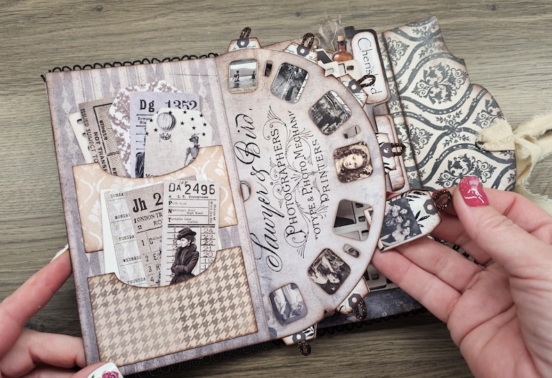 May include: A vintage-style scrapbook with a spiral binding, featuring pockets with old tickets and patterned paper. The cover has a striped design, and a decorative wheel with the text "Sawyer & Bird, Photographers" is visible.