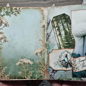 May include: A journal spread featuring a light green background with white yarrow illustrations on the left page. The right page displays a forest scene with birch trees, a fern, a dandelion, and a label with the text Simple Things.