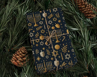 Puede incluir: Un regalo envuelto con un fondo azul marino y símbolos dorados de las fiestas judías, incluyendo menorás, estrellas de David y dreidels. El regalo está atado con hilo y colocado sobre un fondo de agujas de pino y piñas.