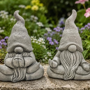 May include: Two gray stone garden gnomes in a seated position. The left gnome has hands pressed together in a prayer gesture, while the right gnome has hands resting on knees in a meditation pose. Both figures wear tall, pointed hats and long beards.