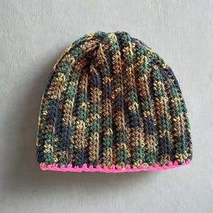 Puede incluir: Un gorro tejido a mano con un patrón de camuflaje y un ribete rosa brillante. El gorro presenta un diseño de punto acanalado en tonos verdes, marrones y azul marino. Este gorro de invierno acogedor es perfecto para actividades al aire libre o uso diario.
