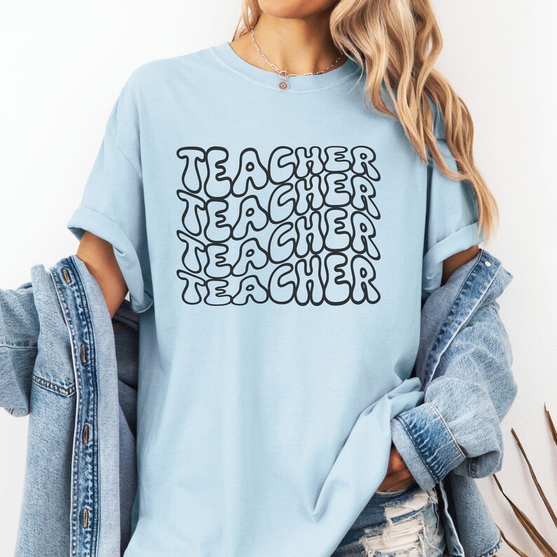 May include: A light blue t-shirt with the word "TEACHER" repeated in a black, bubble-like font.