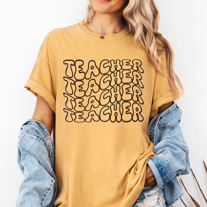 May include: A mustard yellow t-shirt with the word "TEACHER" repeated in a black, bubble-like font.