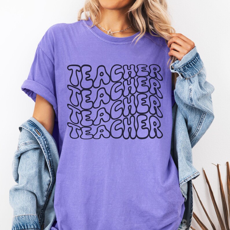 May include: Purple t-shirt with the word "TEACHER" repeated in a retro, bubble-letter style.