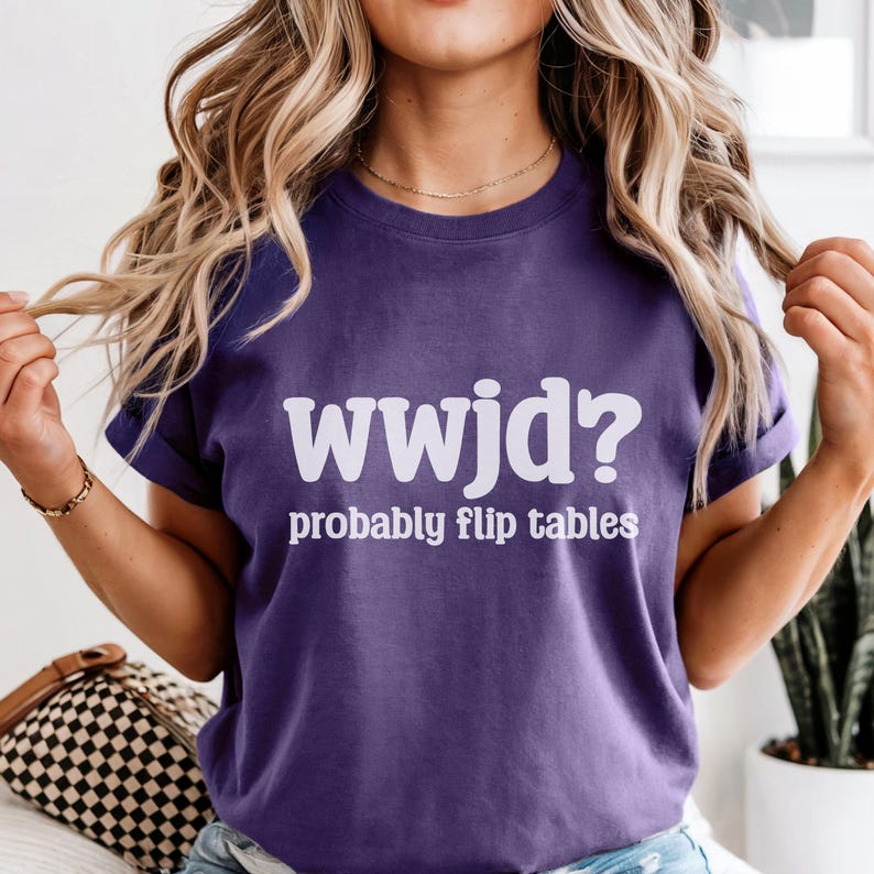 May include: A purple t-shirt with the white text "wwjd? probably flip tables." The shirt has short sleeves and a crew neck. The text is in a bold, sans-serif font.