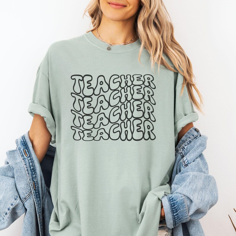 May include: A light green t-shirt with the word "TEACHER" repeated five times in a black, bubble-like font.