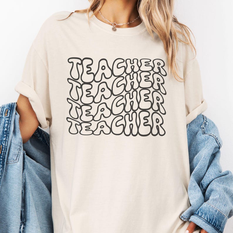 May include: A cream-colored t-shirt with the word "TEACHER" repeated five times in a black, bubble-like font.
