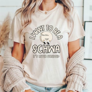 May include: A white t-shirt with a graphic of a cartoon schwa sound with the text "I want to be a schwa it's never stressed".